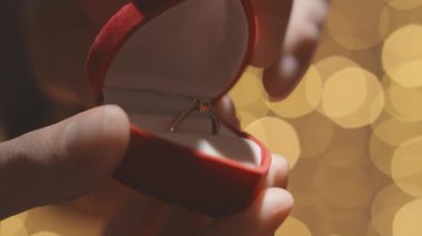 Güzel hazırlanmış bir nişan yüzüğünün yakın plan görüntüsü lüks bir kırmızı kadife kutuda, yumuşak, sıcak bir bokeh arka planla çevrili, samimi bir aşk ve evlenme teklifi anı yakalıyor..