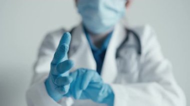 Bir sağlık çalışanı ameliyattan önce mavi eldivenleri dikkatlice giyer ve hasta korumasının gerekli olduğu klinik ortamlarda güvenlik ve hijyenin hayati önemini vurgular.