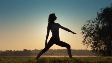 Bir kadın, dinginliği, farkındalığı ve doğanın güzelliğiyle olan derin bağlantısını sembolize eden canlı ve nefes kesici bir gündoğumu sırasında nazikçe yoga yapar.