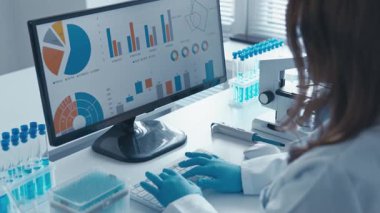 Laboratuvar önlüğü giymiş bir bilim adamı, karmaşık verileri titizlikle bir bilgisayar ekranında analiz ederek, çalışmalarında teknoloji ve biyolojinin önemli kesişimlerini vurguluyor.