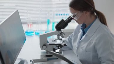 Modern bir laboratuvarda, bir araştırmacı mikroskop altında örnekleri incelerken bilgisayardaki geniş verileri inceleyerek, çalışmalarında bilim ve teknoloji arasındaki önemli bağlantıyı vurguluyor.