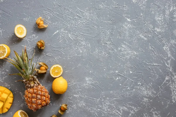 Yellow fruits. Ripe juicy pineapple with mango, physalis and lemons on gray wooden table, top view.
