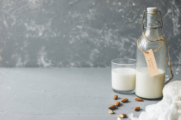 Vegan almond milk in glass bottle with almonds on wooden background with copy space.