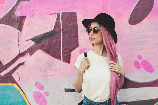 Belle jeune femme hipster élégante avec de longs cheveux roses, chapeau et lunettes de soleil dans la rue . — Photo