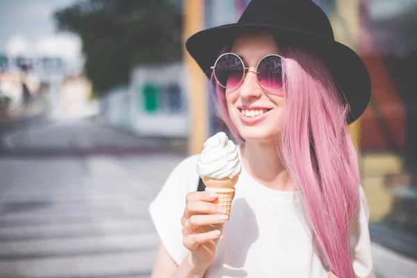 Feliz jovem hipster mulher com cabelos longos rosa, chapéu e óculos de sol comer sorvete ao ar livre — Fotografia de Stock