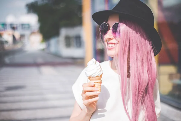 Feliz jovem hipster mulher com cabelos longos rosa, chapéu e óculos de sol comer sorvete ao ar livre — Fotografia de Stock