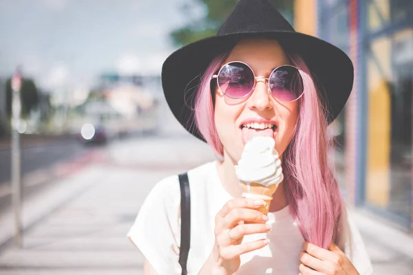 Feliz jovem hipster mulher com cabelos longos rosa, chapéu e óculos de sol comer sorvete ao ar livre — Fotografia de Stock