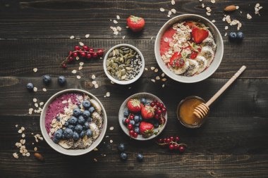 Helthy kahvaltı. Güler yüzlü lezzetli meyve, çilek ve tohumlar ahşap arka plan üzerinde kaseler.