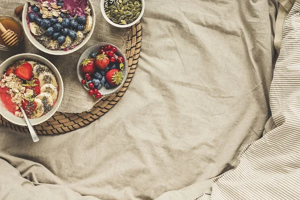 Desayuno tranquilo en la cama. Deliciosos tazones de batido con bayas, frutas y semillas, vista superior. Fondo con espacio de copia — Foto de Stock