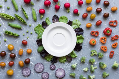 Tablo üzerinde beyaz plaka ile taze organik sebze. Yeşil bezelye, brokoli, soğan, domates, turp üstten görünüm.