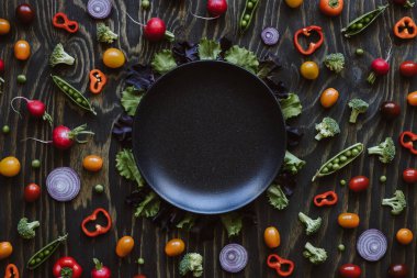 Ahşap masa üzerinde siyah plaka ile taze organik sebze. Yeşil bezelye, brokoli, soğan, domates, turp ahşap masa üzerinde. Üstten görünüm.