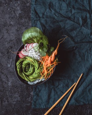 Pirinç Noodle, havuç, turp ve siyah arka plan üzerine avokado ile çiğ vegan kase. Üstten görünüm