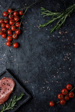 Siyah arka plan üstten görünüm üzerinde biberiye ve domates ile çiğ Dana kaburga eti. Kopya alanı ile.