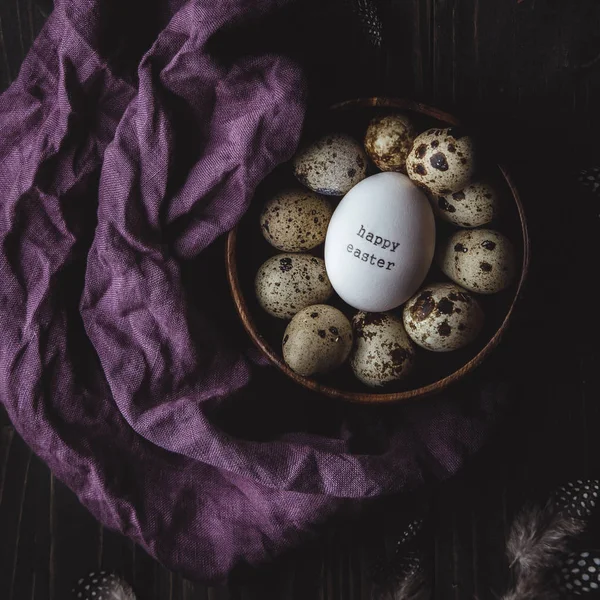 Gelukkige Pasen. Happy Easter Egg met kwarteleitjes in houten kom op donkere houten achtergrond. — Stockfoto