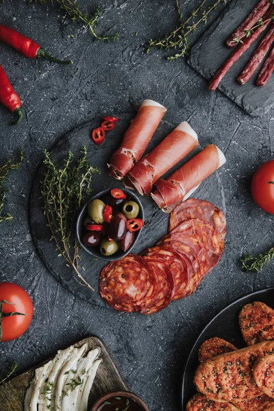 Mistura de aperitivos mediterrâneos. Jamon, chouriço, fuet e filetes de anchova no fundo escuro vista superior . Fotos De Bancos De Imagens Sem Royalties