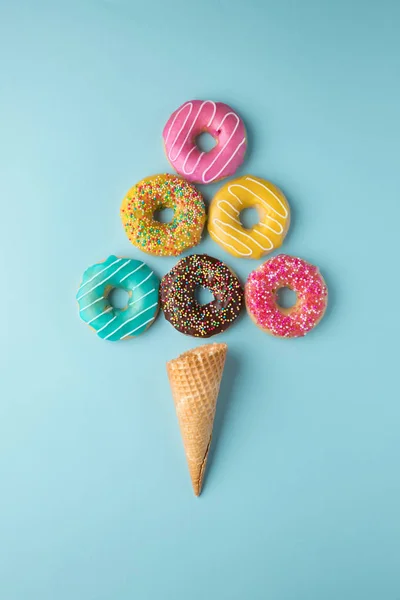 Sorvete feito de donuts coloridos e cone de waffle no fundo azul claro . Fotos De Bancos De Imagens