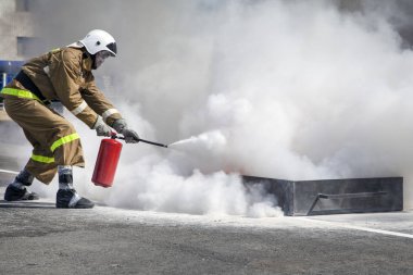 Büyük bir yangını söndürmek. Özel takım elbiseli profesyonel bir itfaiyeci yangın söndürücüyle yangını söndürüyor. İtfaiyecileri yangını söndürmek için eğitiyorum.