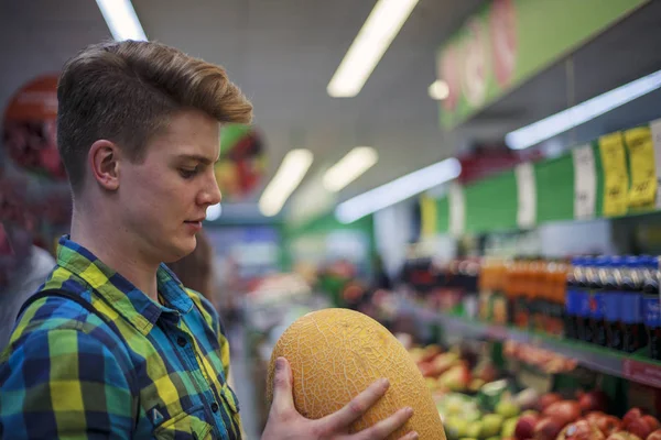 A young man in a shop, chooses melon