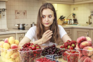 Güzel genç kız mutfakta meyve ve taze çilek yiyor