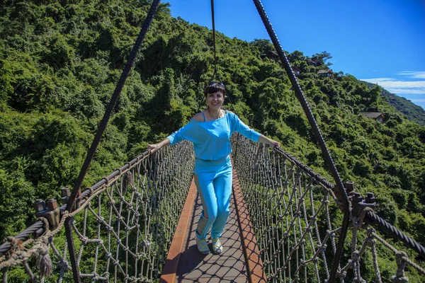 Tourists are walking on a wooden suspension bridge in the park of Yalong Bay Tropic Paradise Forest.