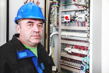 Elektrik kabininin yakınındaki elektrotamirci, bir elektrikçi bir elektrogüç kurulumunun kontrol kabinini denetler