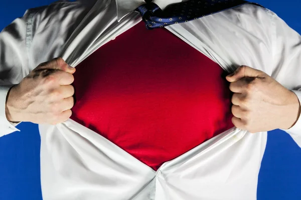 Businessman tearing off his suit on blue background, man pushes shirt with red t-shirt. Superhero.