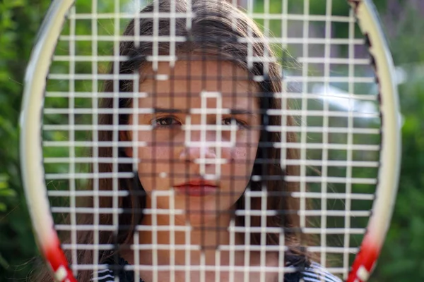 Young girl looks through tennis racket, — Stock Photo, Image