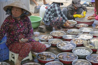 Mui Ne, Vietnam-7 Temmuz 2019: Balıkçı köyü. Sokak satıcıları geleneksel şapkalarla bisikletlerinden meyve satar, kadın deniz ürünleri, küçük yengeçler satar.