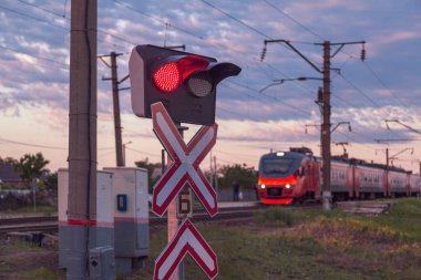Tehlikeli kontrolsüz demiryolu geçişi, kırmızı trafik ışığı, hareket eden tren, alacakaranlıkta görüş mesafesi zayıf.