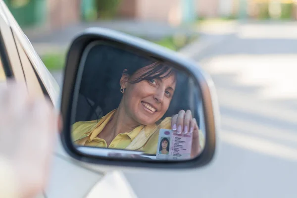 Getting a driver\'s license, a beautiful driving girl shows a new driver\'s license. Young woman holding driving license near open car.