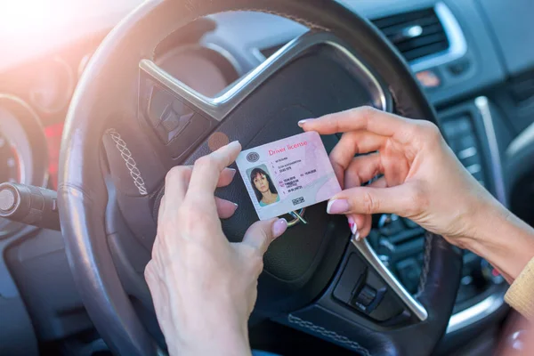 获得驾驶执照时 女性的手在汽车的方向盘上展示美国的驾驶执照 — 图库照片