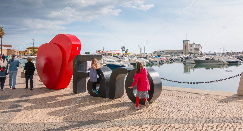 Faro, Portugal - May 1, 2018: Faro city logo name with big letters near the marina in front of which tourists take pictures on a spring day
