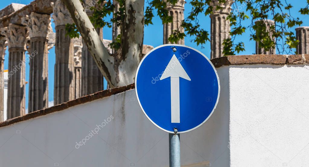 Blue round road sign ahead only in front of the ruins of a Roman temple of Evora