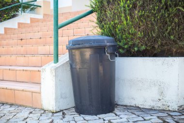 Siyah plastik bahçe çöp tenekesi bir evin girişinin önünde.
