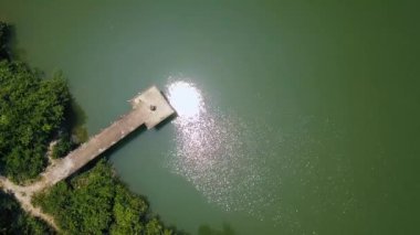 Güneş yansıma yeşil su ve iskele göster casus uçak uçan. Göl kıyısı tekneler için havadan görünümü iskele.