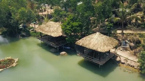 夏の休息のための熱帯の自然の中の緑の水と山の湖の海岸の茅葺き屋根の家します。湖岸ドローン ビューで夏の床の間. — ストック動画