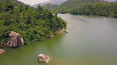 Temiz yeşil suyu ve kıyı manzarasında büyük taşları olan güzel bir dağ gölü. Kıyı şeridinde uçan drone oyuğundan manzara. Yeşil dağların arasında kayalık nehir..