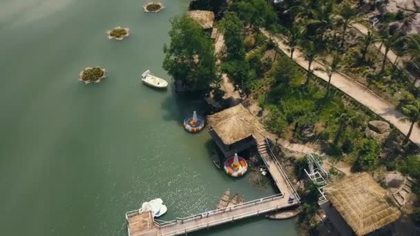 Bungalow esotici con tetto di paglia e molo barca sulla riva verde vista aerea lago. Cottage vacanze vista drone sul lago tropicale riva tra natura esotica . — Video Stock