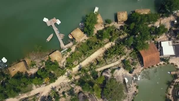 Aerial shoot boat pier and bungalow for rest on lake among tropical nature on island. Green water in beautiful lake and palm trees drone view. — Stock Video