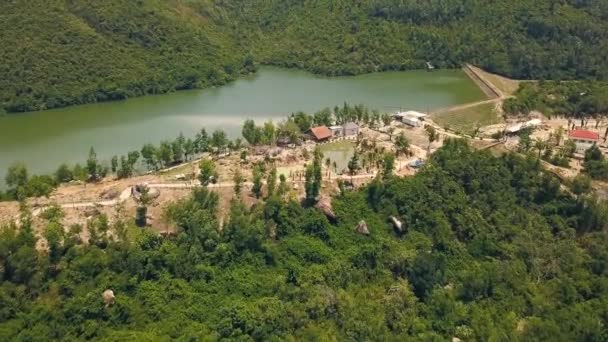 Imágenes aéreas del río y la presa de montaña. Casas y alcoba con techo de paja en la orilla en el lago de montaña con brote aéreo de agua verde de dron volador . — Vídeos de Stock