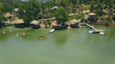 Ahşap Bungalov resort otel sahil yeşil göl thatched çatı ve tekne rıhtımda görünümü robot. Evler kıyı dağ gölü su villa resort hava manzara vahşi doğada arasında.