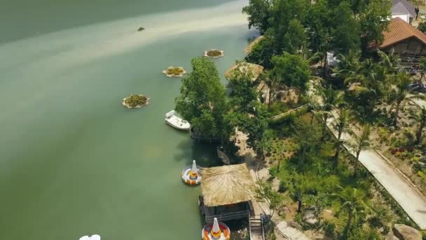 Bungalows avec toit de chaume et jetée en bois pour les bateaux sur le rivage lac vert dans la vue de drone hôtel de montagne de luxe. Chalets au bord du lac tropical au milieu de la nature exotique dans l'eau villa resort images aériennes — Video