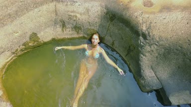 Rahatlatıcı kadın şeffaf nehir su üstten görünüm içinde banyo. Genç kadın arka plan büyük taşlar havadan görüntüleri nehir suda yüzmek. Havadan görünümü kız nehirde Yüzme.