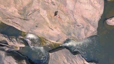 Nehir kıyısında havadan görünümü üzerinde büyük taş üzerinde oturan Bikini güzel bir kadın. Dinlenme ve nehir su dron çekimi büyük kayanın üzerinde rahatlatıcı genç kadın.