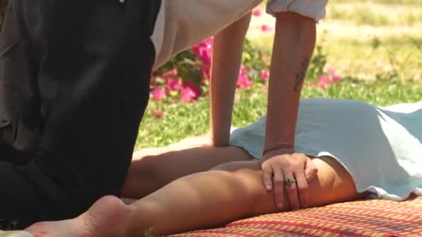 Hombre masajista haciendo yoga masaje a mujer acostada sobre hierba verde al aire libre. Hombre masajista profesional haciendo masaje tailandés a mujer joven. Estilo de vida saludable . — Vídeo de stock