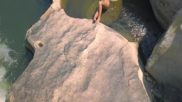 Молодая женщина в купальнике лежит на большом камне в речном беспилотнике. Женщина отдыхает и загорает на скале с видом на реку — стоковое видео
