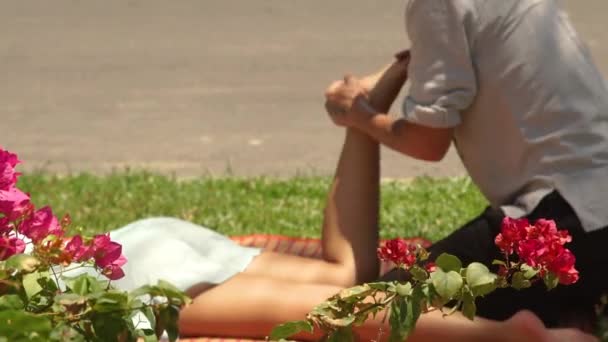 Мужчина тайский массажист делает массаж ног женщине на открытом воздухе. Тайский массажист делает растягивающий йога массаж женской ноги. Здоровый и гармоничный концепт . — стоковое видео