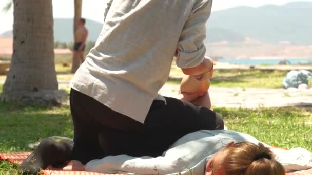 Tailandés masajista haciendo estiramiento masaje de pierna femenina al aire libre. Mujeres recibiendo curso de yoga masaje. Concepto de tratamiento y rehabilitación . — Vídeos de Stock