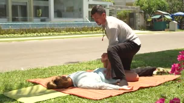 Yoga masagiste haciendo estiramiento masaje de pierna femenina al aire libre. Masaje tailandés profesional para la relajación y la recuperación de la salud. Tratamiento y concepto de curación . — Vídeos de Stock