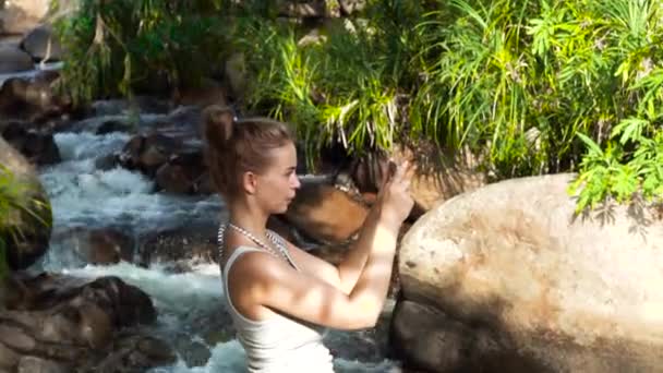 Toeristische vrouw doen foto wilde natuur op mobiele telefoon tijdens het klimmen in berg waterval in regenwoud. Reizende vrouw toeristische schieten video op smartphone tijdens het wandelen op de berg rivier. — Stockvideo